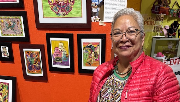 A woman stands next to a display of colorful, framed popotillo artworks.