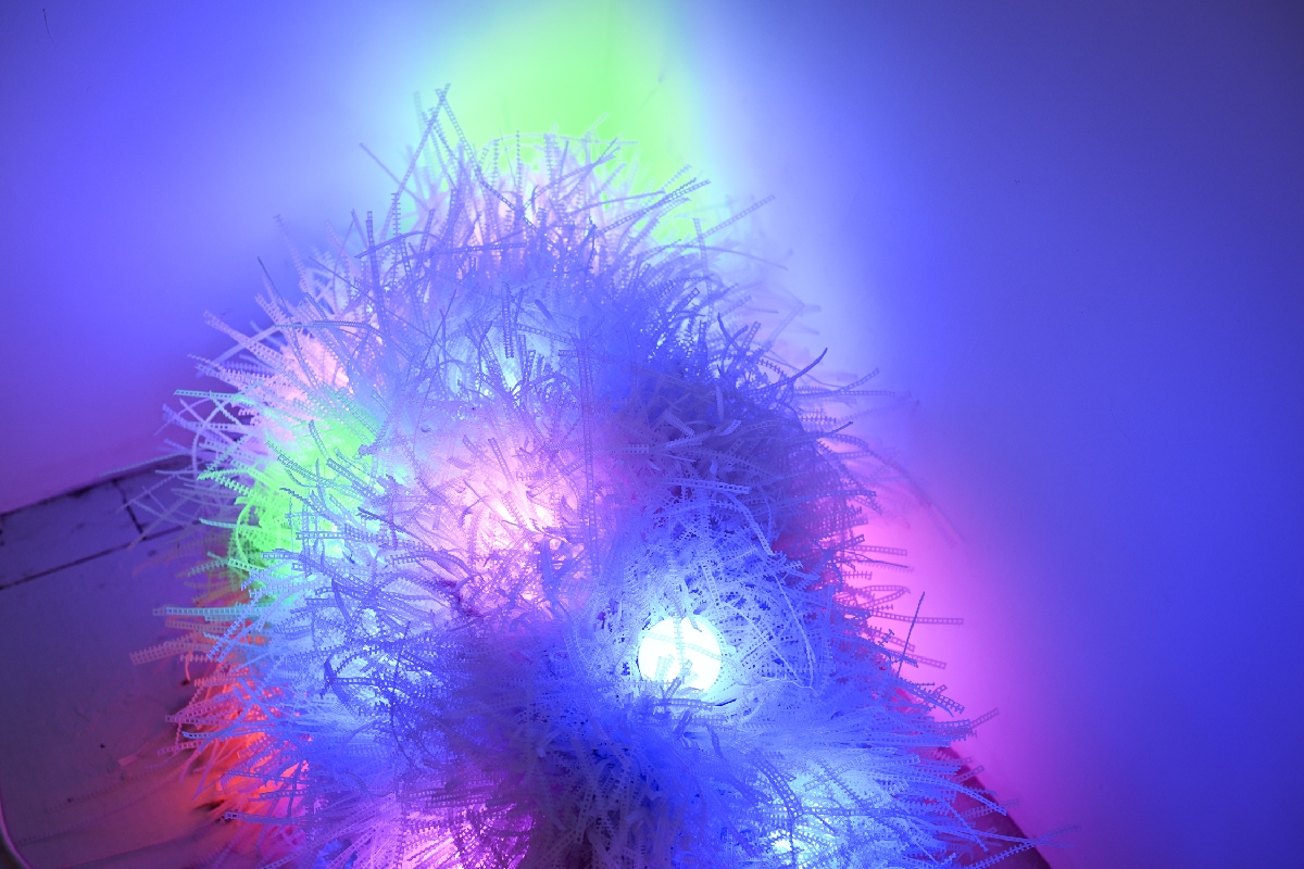 Multi-color orb lights in green, blue, and pink light up a fuzzy shape next to a wall.