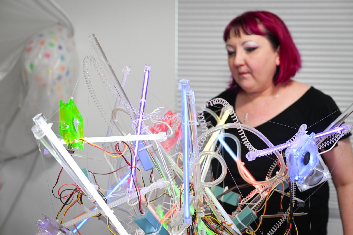 Adela looks at her sculpture of rods and springs mixed with multicolor neon lighting.