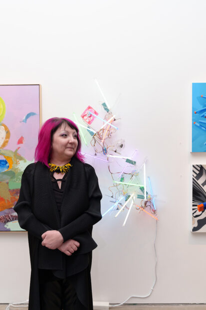 A photograph of artist Adela Andea standing in front of her light art work at a gallery.