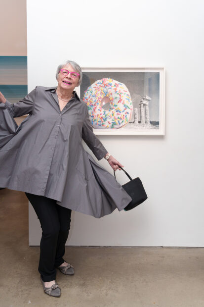 A photograph of artist Neva Mikulicz playfully posing with her framed photograph of a monumental donut.